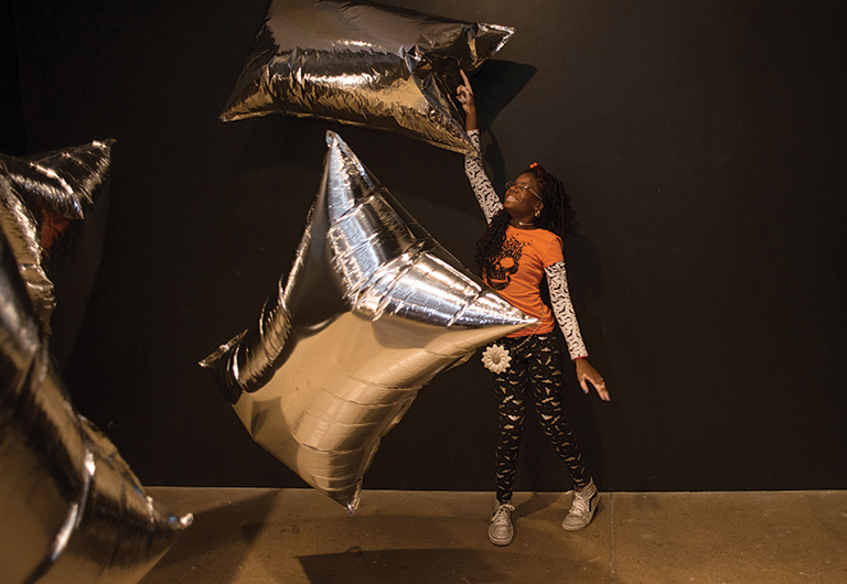 young girl jumping up and playing with silver metallic balloons