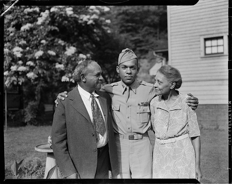 soldier posed with arms around man wearing paisley tie and woman wearing floral dress, possibly his parents in 1944 