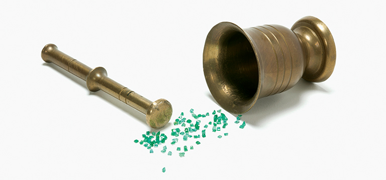 A pestle and mortar laying on its side with green emeralds spilling out of it.