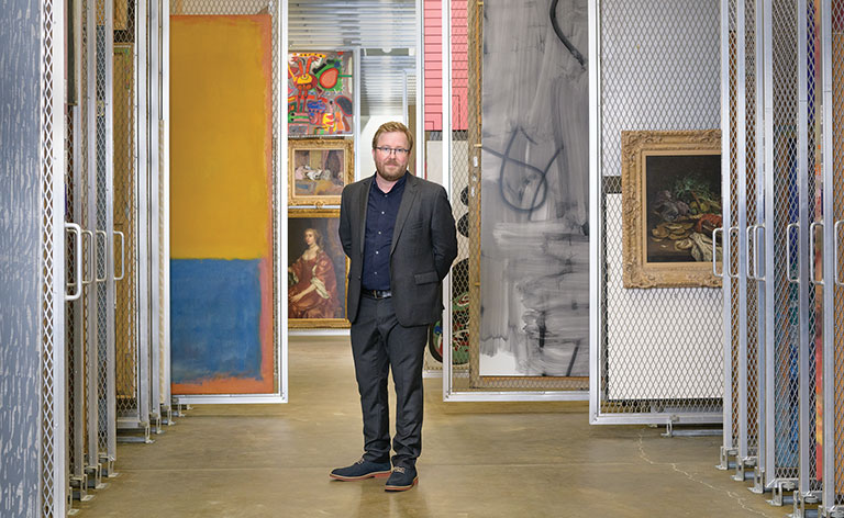 Eric Crosby standing among painting in museum storage