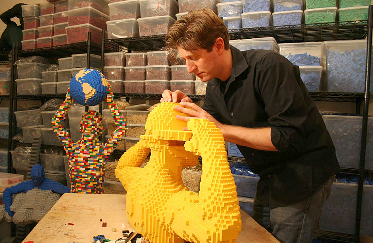 Artist working in his studio surrounded by bins of lego bricks