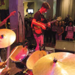 A group of teens in a band playing music on a stage at the Warhol museum