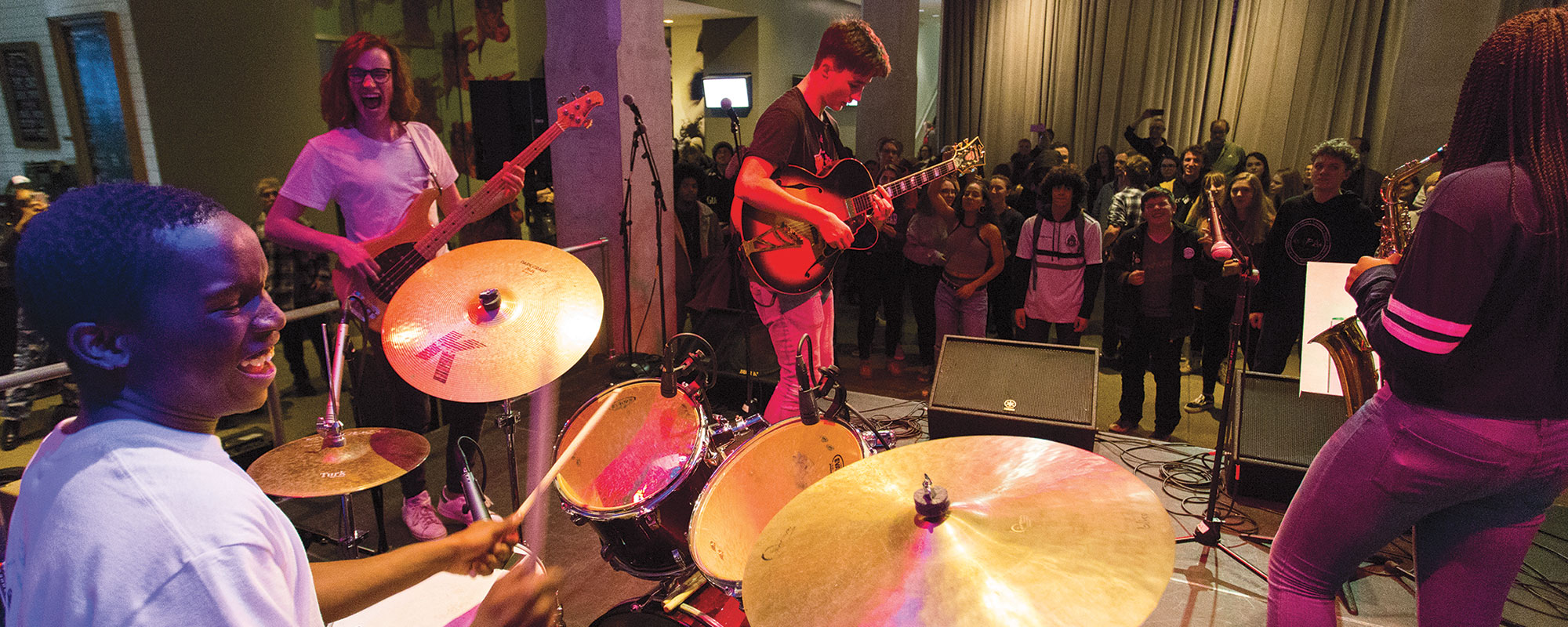 A group of teens in a band playing music on a stage at the Warhol museum