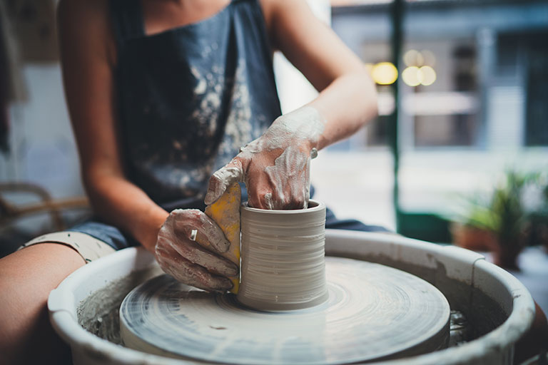 A photo of a woman throwing a pot on a potters wheel working on a