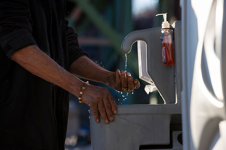 A man washing his hands at an outdoor water fountain.