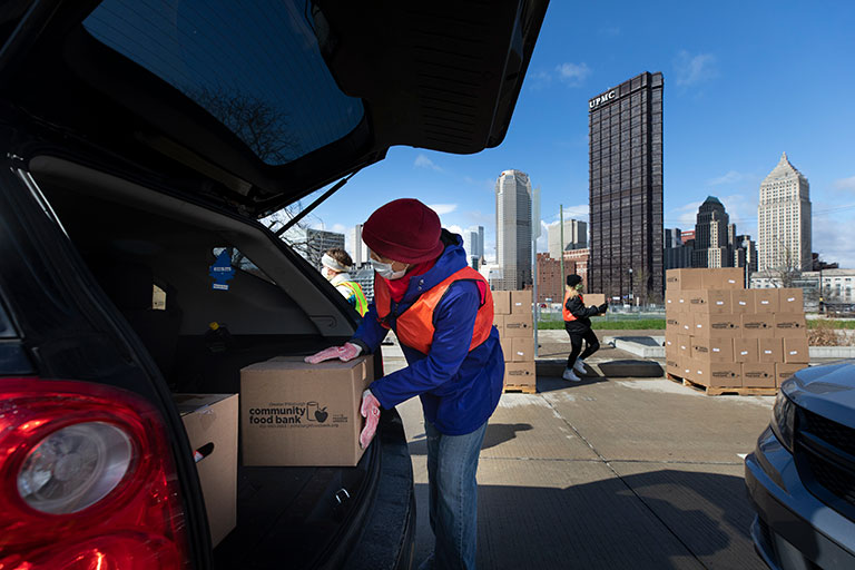 A women loading boxes of food into the back of a car.