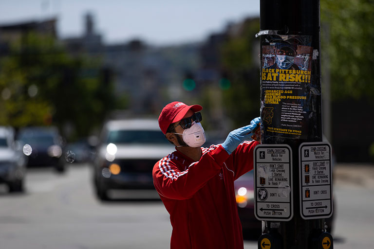 A man posting an education poster wearing a mask.