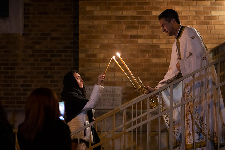 A priest lighting a candle of a women during easter service