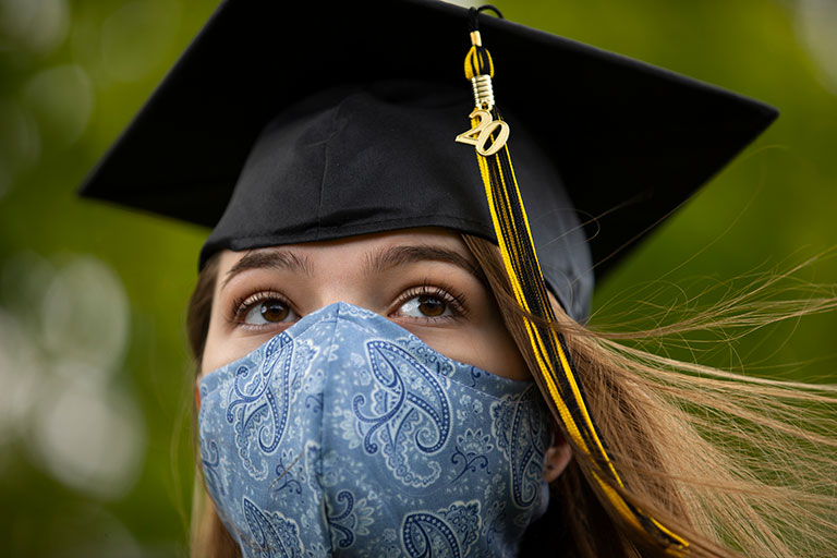 Young girl in graduation cap and wearing a mask.
