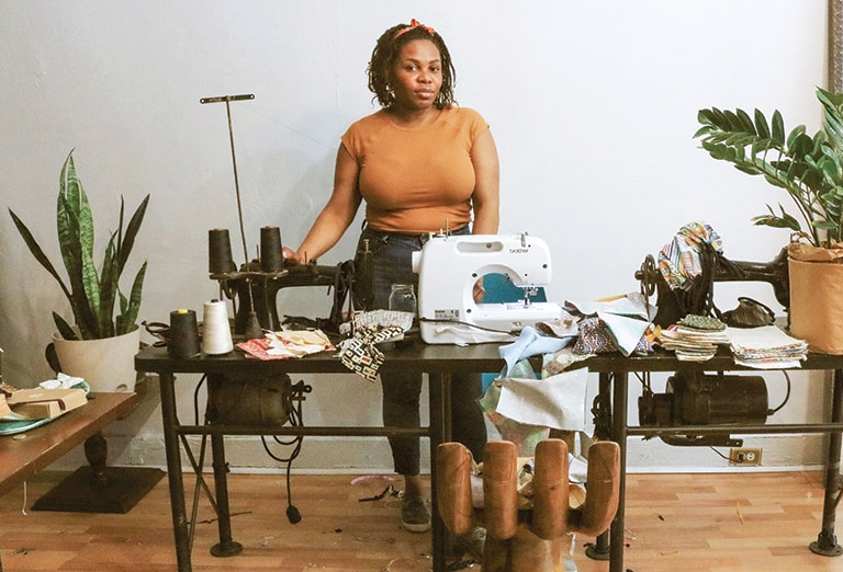 A seamstress standing behind her sewing machine in her studio.
