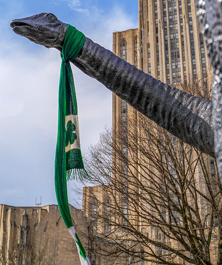 A photo of Dippy the dinosaur wearing a green St. Patrick's scarf.