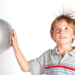 A young boy with his hand on a generator, his hair is sticking up from the static electricity