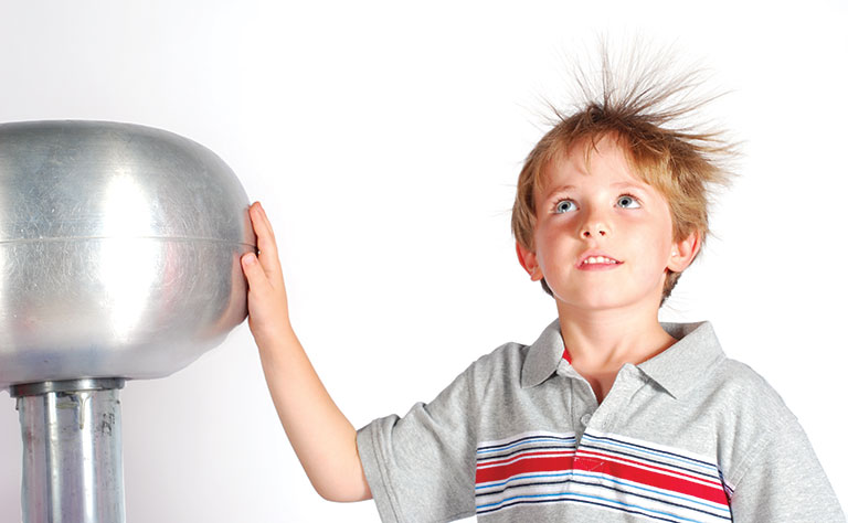 A young boy with his hand on a generator, his hair is sticking up from the static electricity