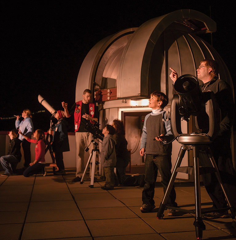 A group of people standing on the roof of a building next to a telescope and observatory