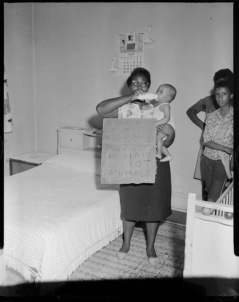 Daisy curry feeding a bottle to her son while wearing a cardboard sign.
