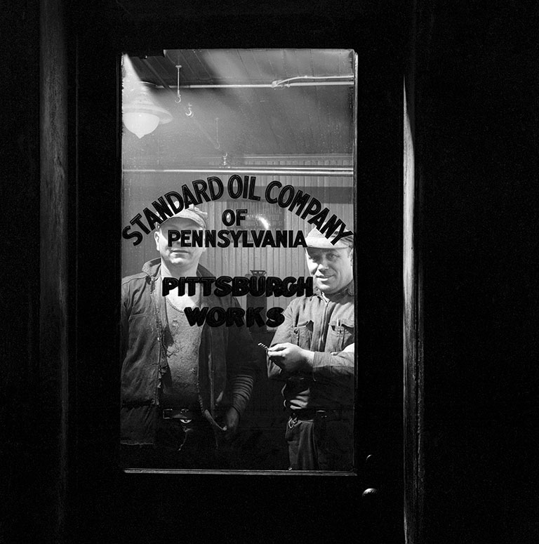 2 men standing behind a glass door that reads Standard Oil Company of Pennsylvania.