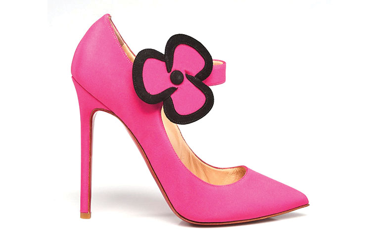 A pink, high-heeled shoe with a large flower shaped buckle