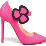 A pink, high-heeled shoe with a large flower shaped buckle