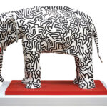 A large plaster elephant with black figures painted on it.