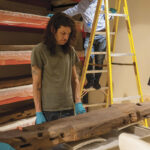 Three museum workers moving a large wooden beam.