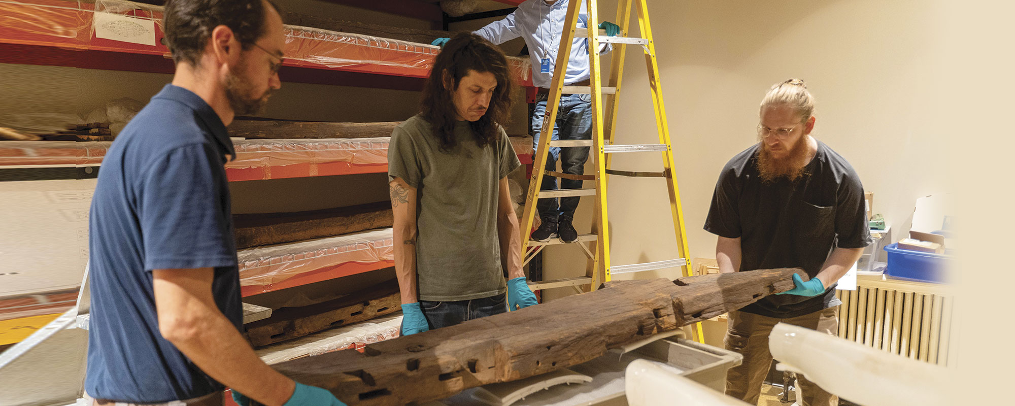 Three museum workers moving a large wooden beam.