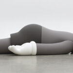 A monotone gray figure laying face down on a floor.