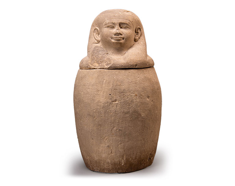 An egyptian artifact with a human head atop of a vessel.