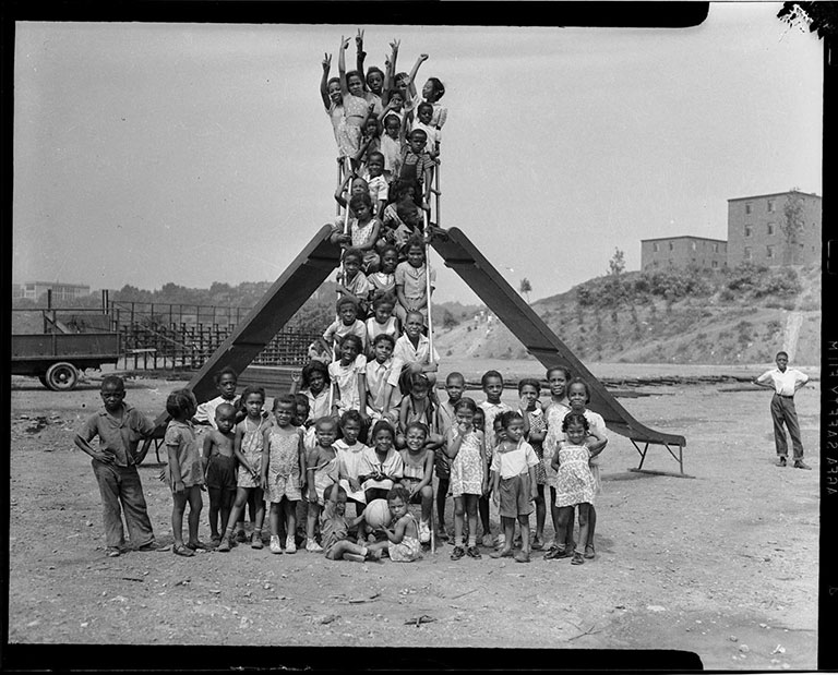 A group of children in a playground making the V sign posing by a sliding board