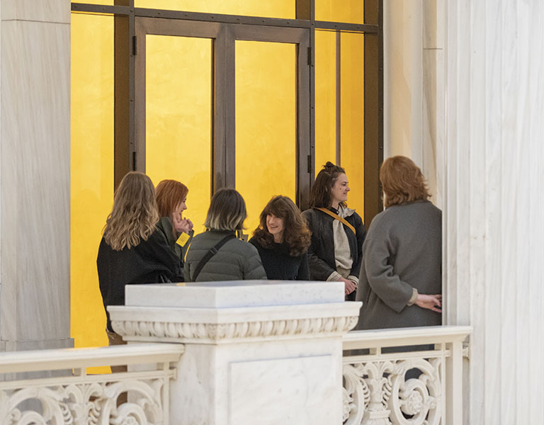 Group of people converse near a striking yellow-lit entrance, framed by elegant marble architecture.