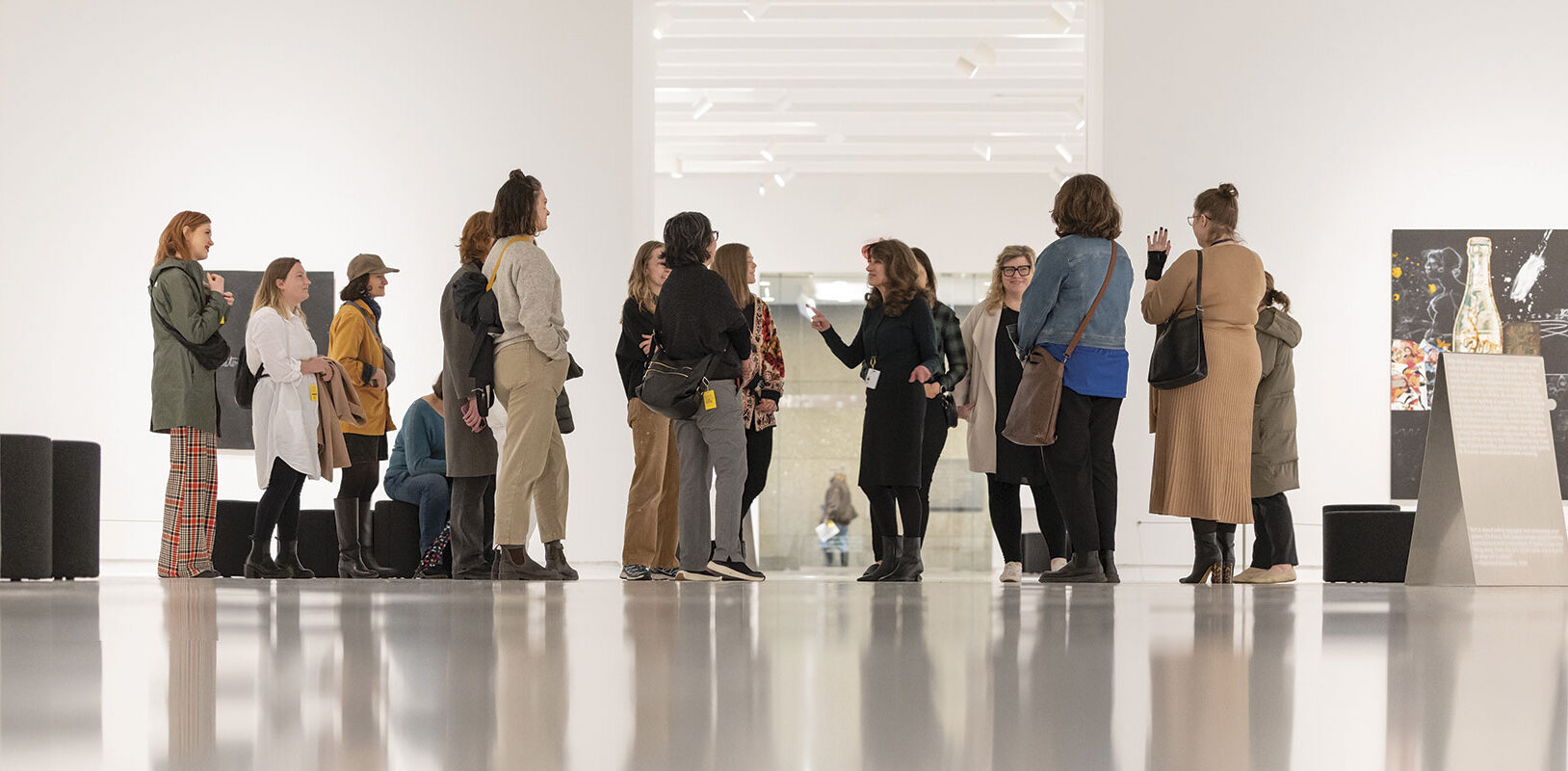 A group of visitors attentively listening to a guide in a bright art gallery, surrounded by modern artwork and sleek white walls.