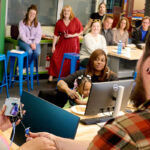 A diverse group of individuals engaged in a learning or collaborative environment, with computers and colorful seating in the background.