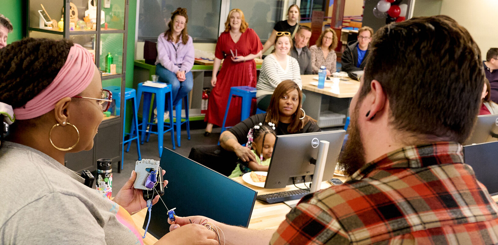 A diverse group of individuals engaged in a learning or collaborative environment, with computers and colorful seating in the background.