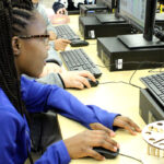 A young girl in a blue shirt working on a computer.