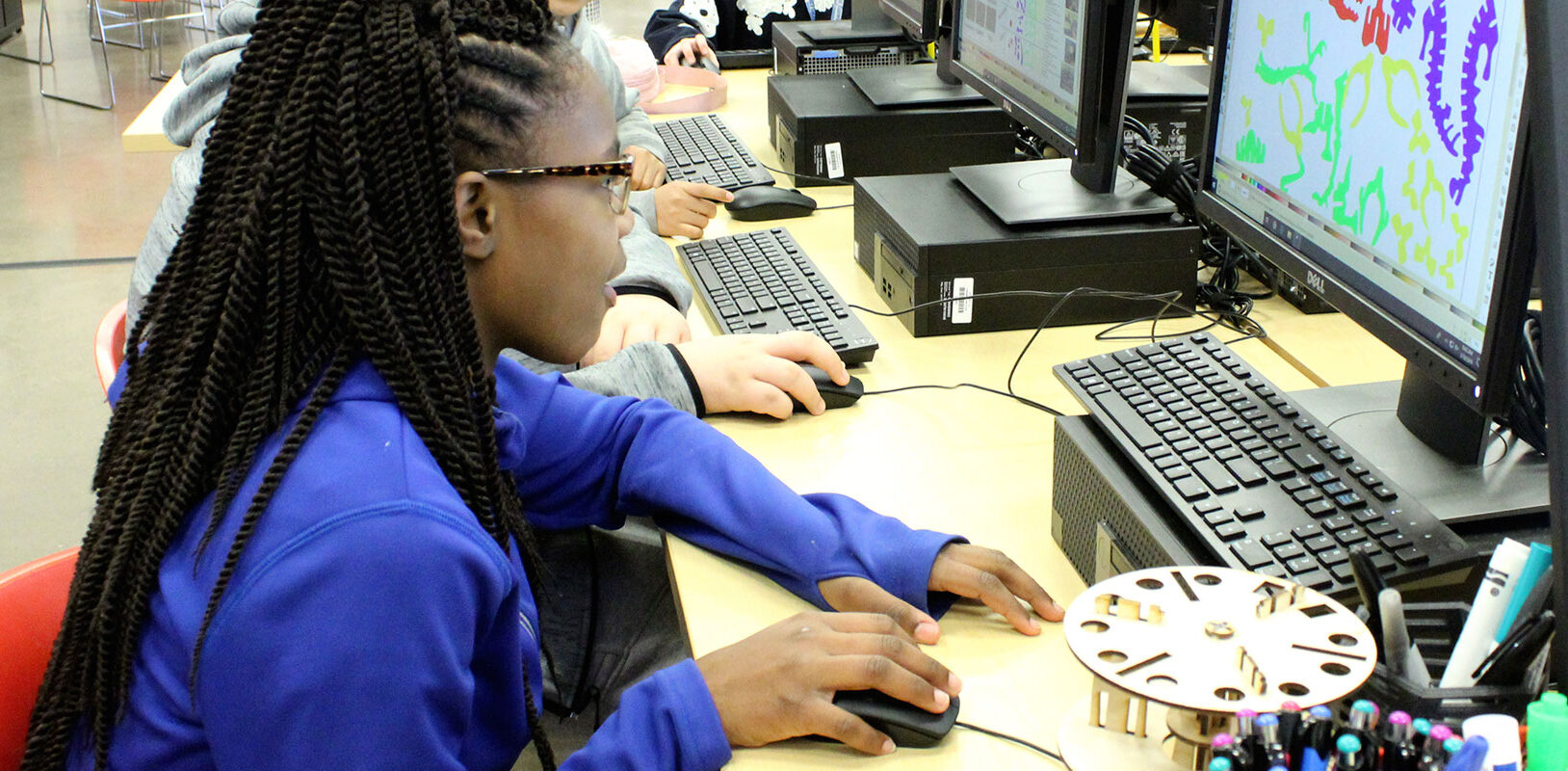 A young girl in a blue shirt working on a computer.