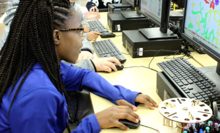 A young girl in a blue shirt working on a computer.