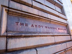 Close-up of the entrance sign for The Andy Warhol Museum, featuring textured stone and bold red lettering.