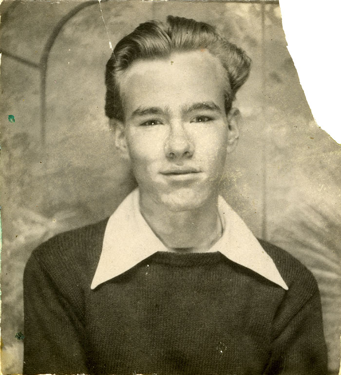 A vintage black-and-white portrait of a young man wearing a dark sweater with a white collar, seated against a textured backdrop.