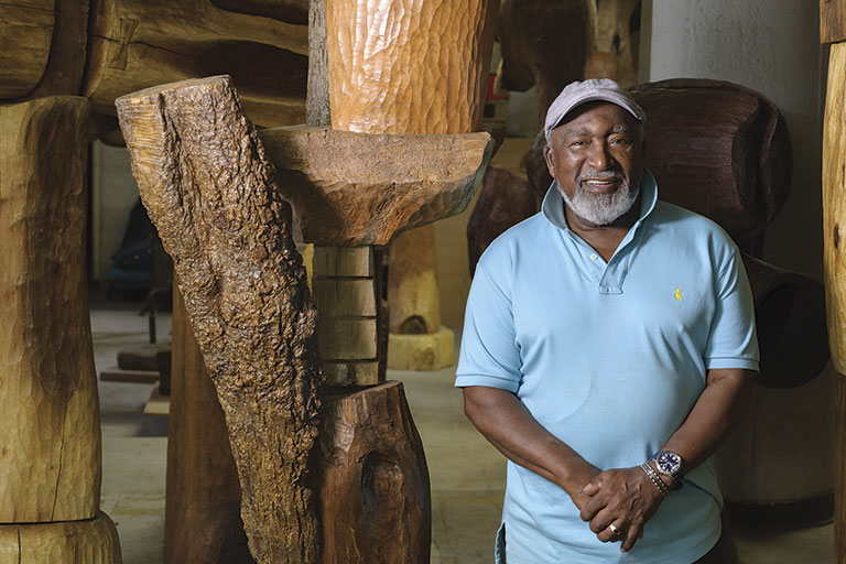 Man standing beside wooden sculpture in workshop