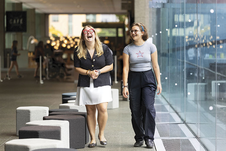 Two young women laughing together in a museum setting
