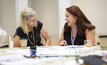 Two women in black tops sitting at a table with papers and coffee