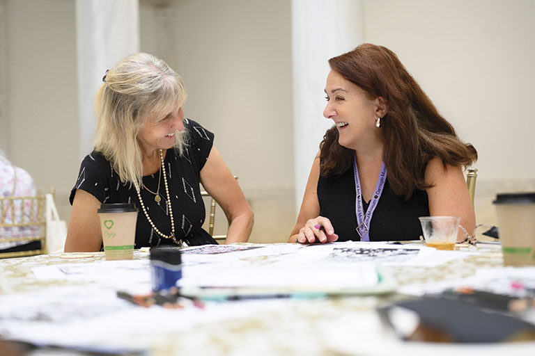 Two women in black tops sitting at a table with papers and coffee
