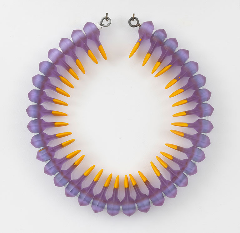A circular necklace featuring translucent purple beads with bright orange spikes, arranged symmetrically. The design is bold and modern.