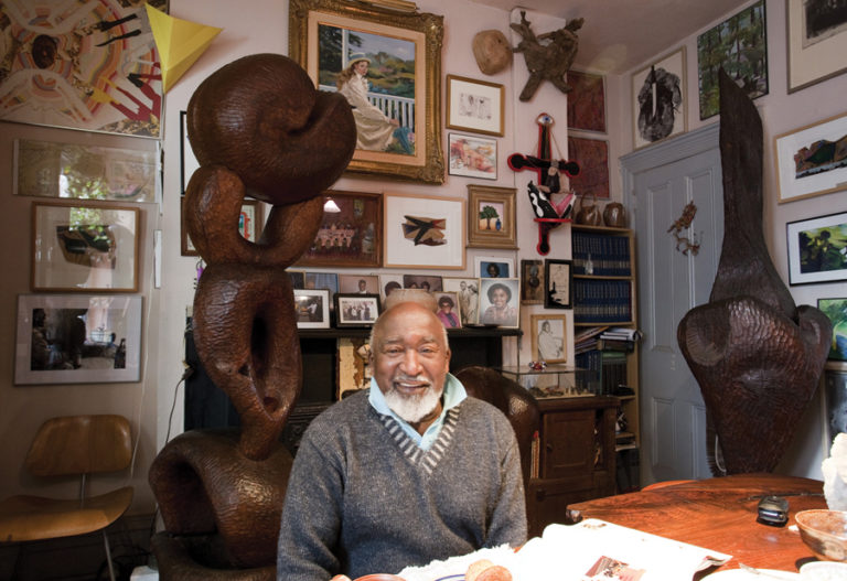 Artist sitting at a table in his home surrounded by artwork