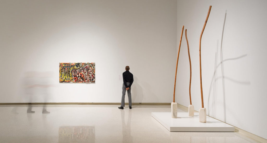 man standing in an art gallery with a scultpture and a painting