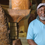 Artist standing in front of large wooden sculptures