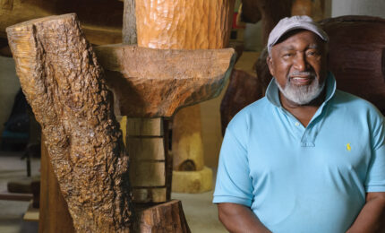 Artist standing in front of large wooden sculptures