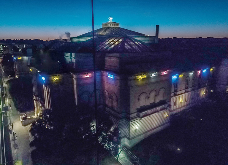 An overhead nightime view of the musem building showing the neon names that wrap around the top of the building.