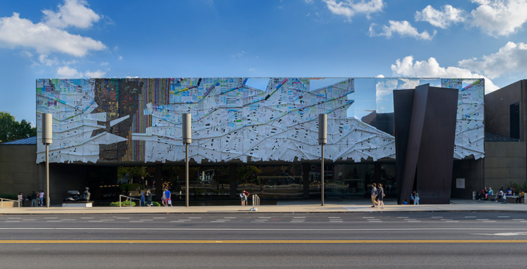 AN exterior view of the museum of Art with an abstract scultpure covering the facade.