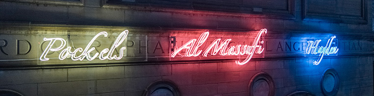 Colorful neon signs mounted to the exterior of the museum building spelling out various names 