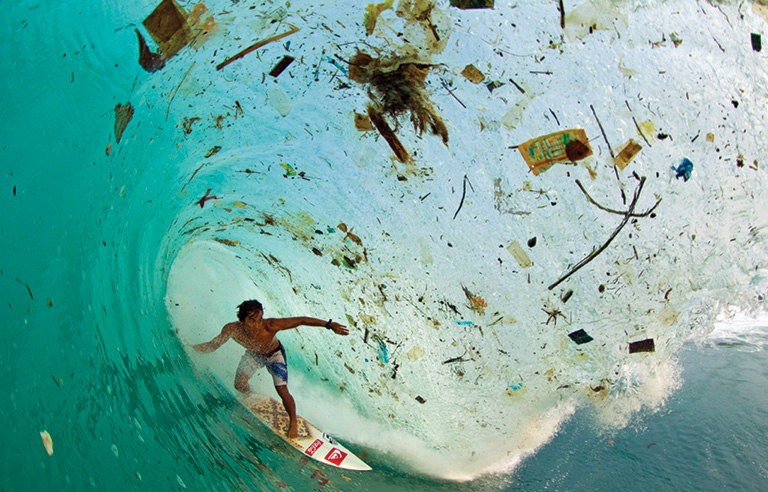 A surfer in a wave filled with plastic and garbage.